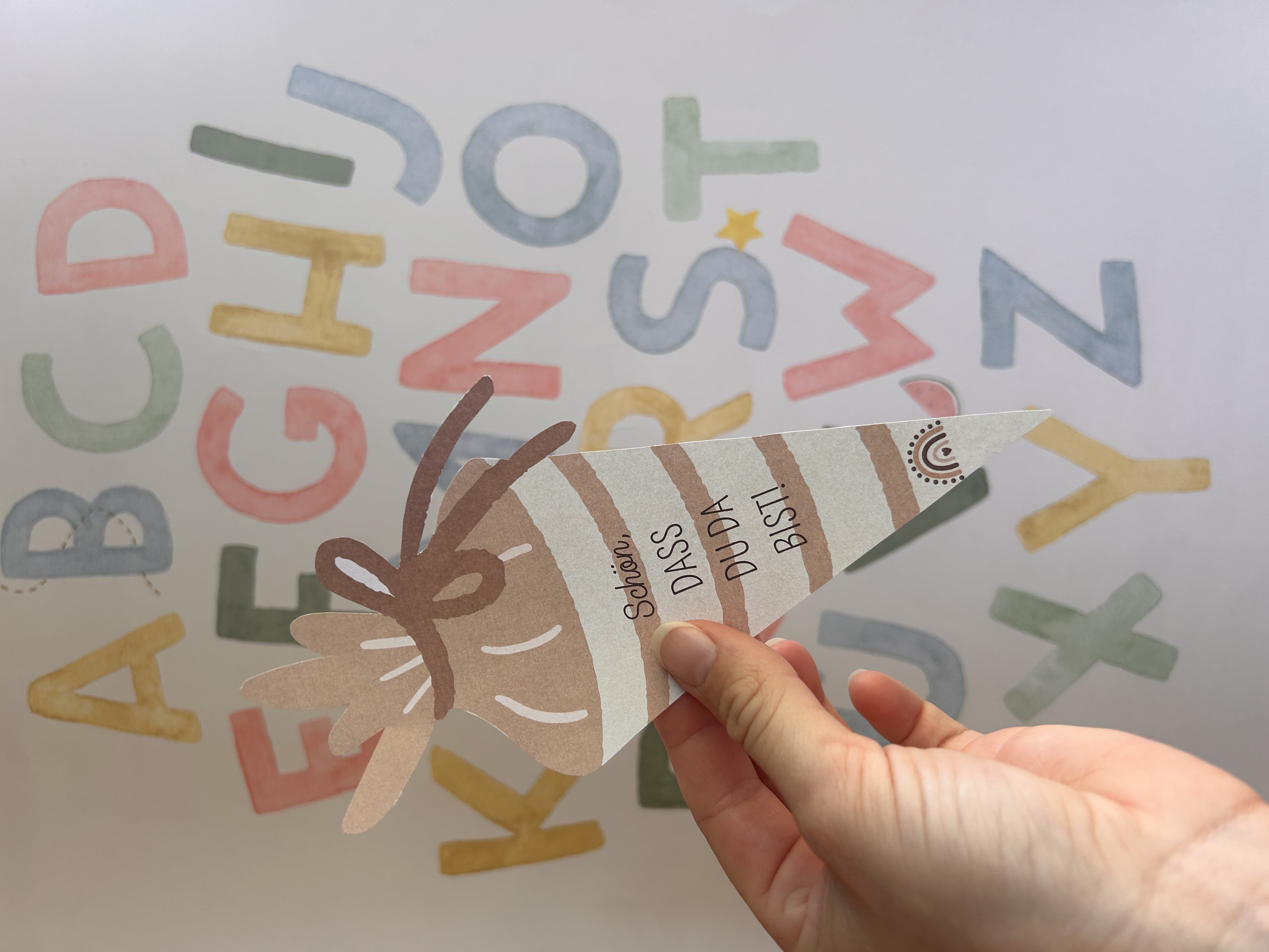 Kleine Schultüte vor einem bunten Hintergrund mit Buchstaben